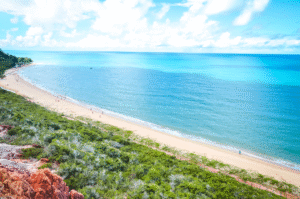 Vista panorâmica da praia de Arraial d’Ajuda com mar calmo e vegetação ao fundo.
